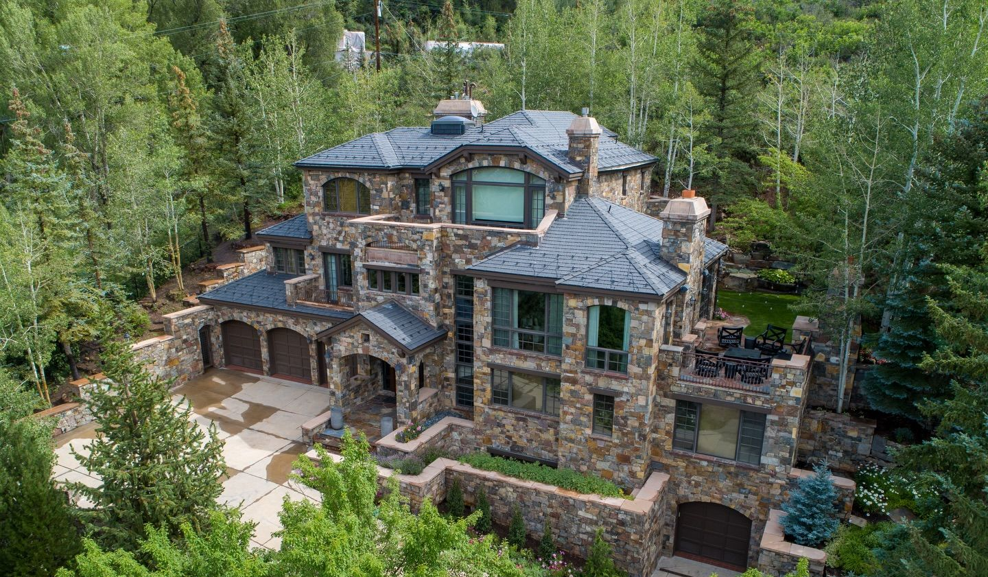 Large stone mansion with a blue roof nestled in dense green forest greenery