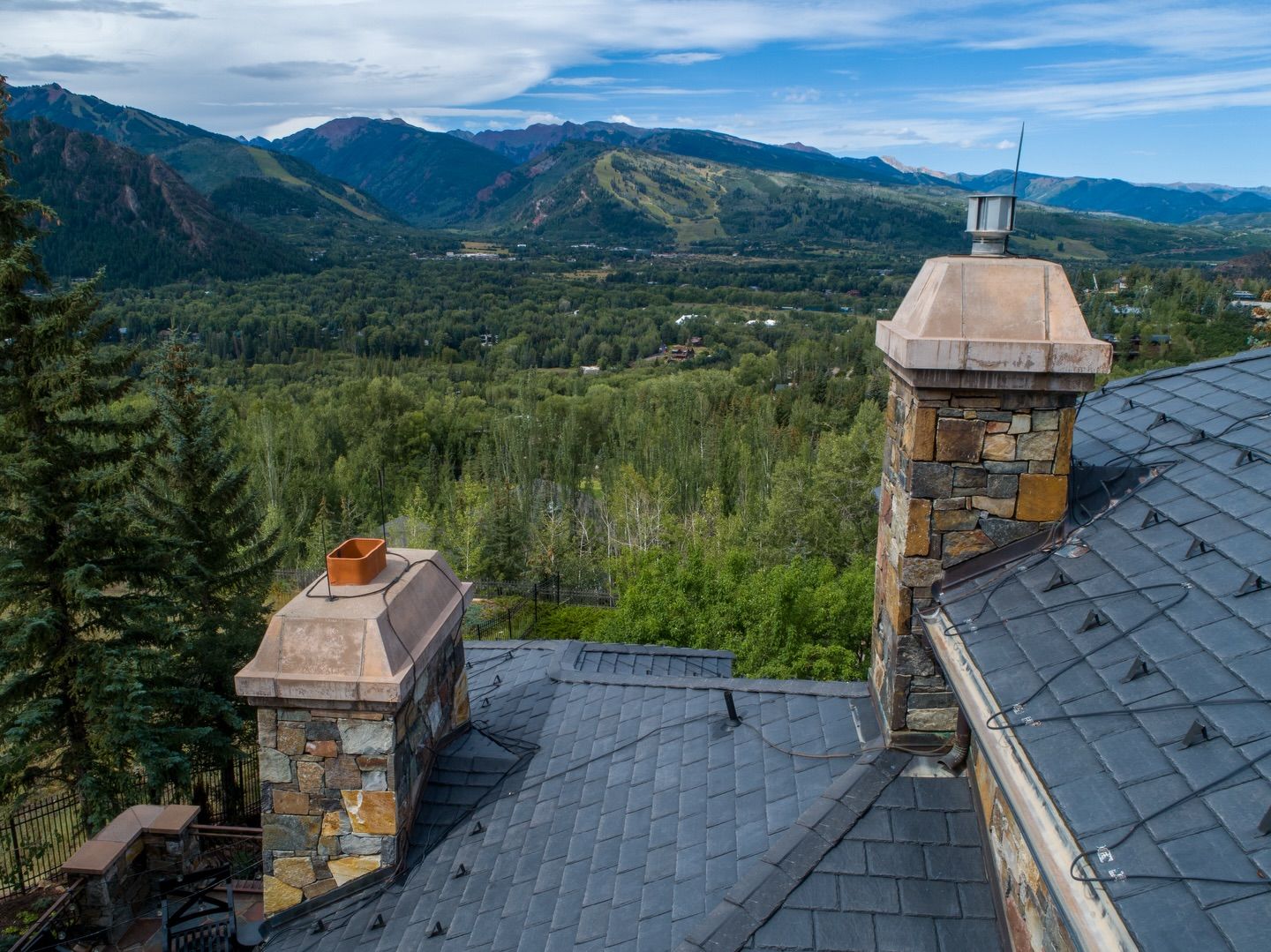 Mountain lodge rooftop overlooking a green forested valley and distant hills under a blue sky