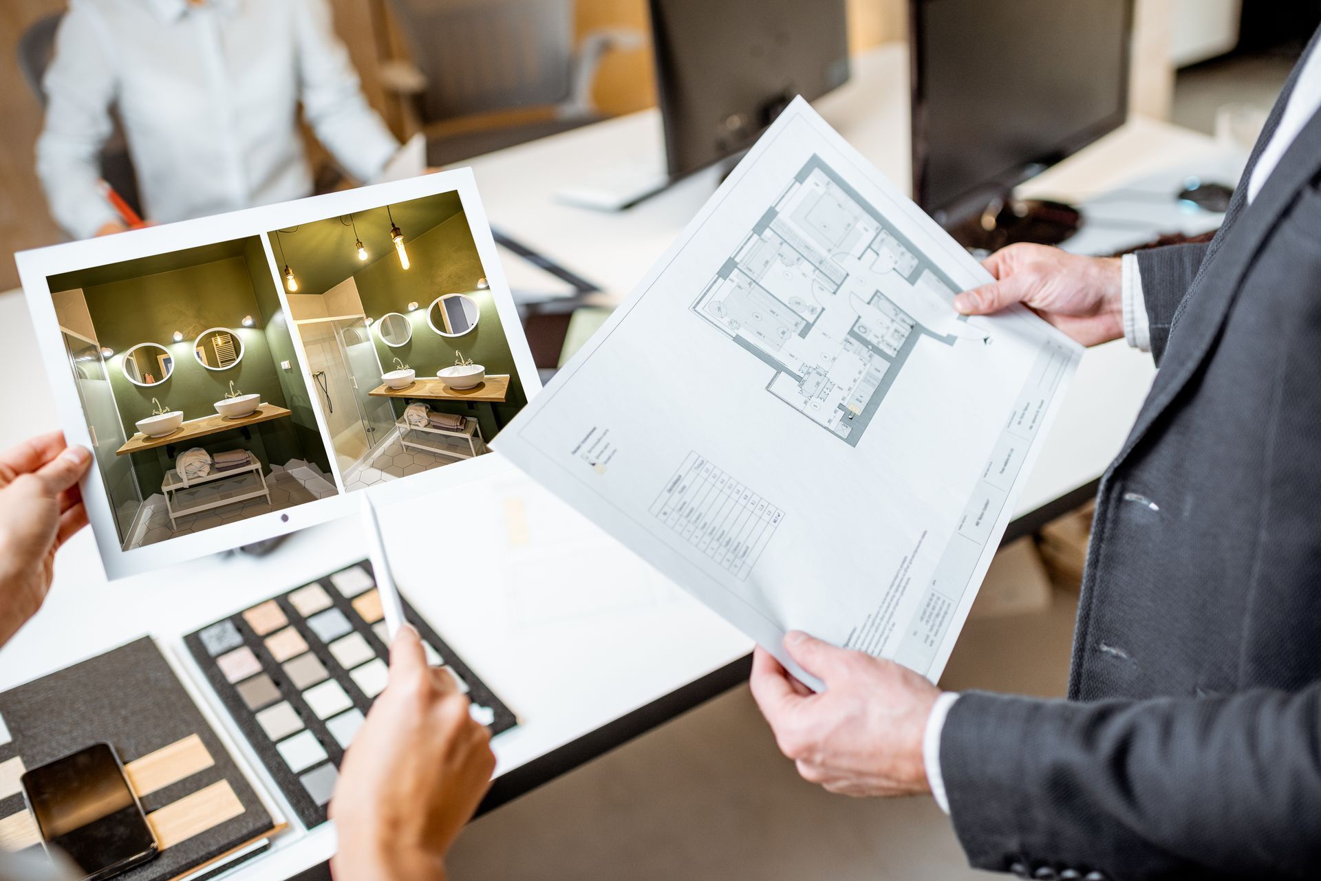 A cropped view of two architects holding plans and blue prints for a bathroom remodel.