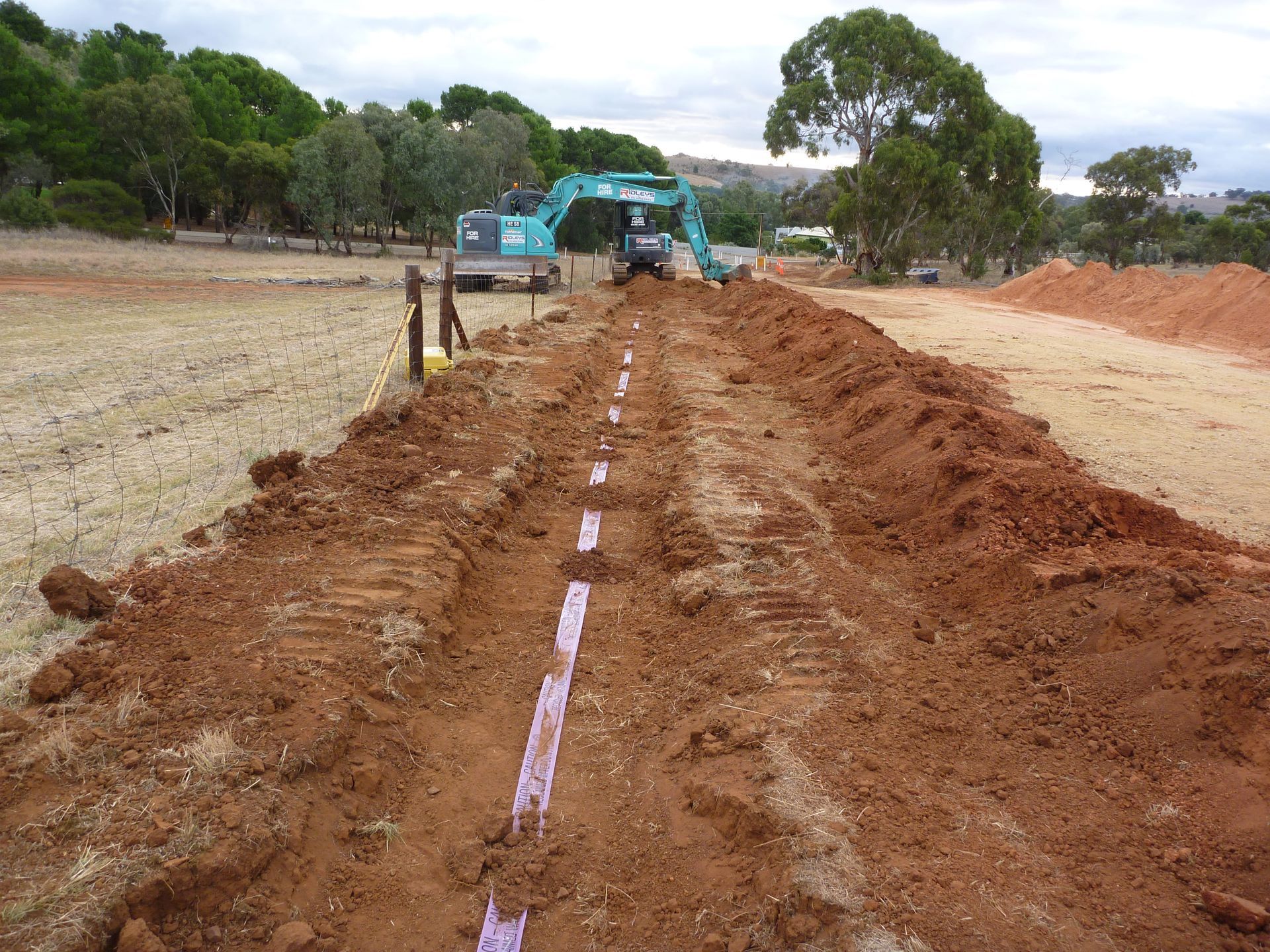 A kobelco excavator is digging a trench in the dirt | Murray Bridge, SA | Ridleys SA