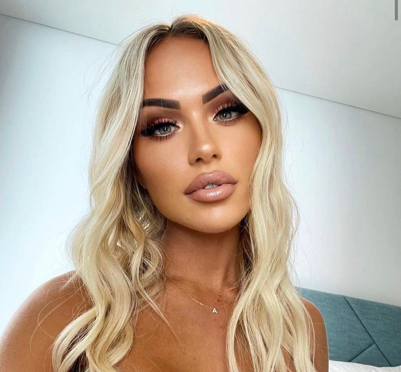 A woman with blonde hair and blue eyes is taking a selfie in a bedroom — Sibina Cosmetic Tattoo Art In Broadbeach, QLD