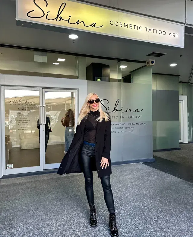 A woman in a black coat is standing in front of a building — Sibina Cosmetic Tattoo Art In Broadbeach, QLD