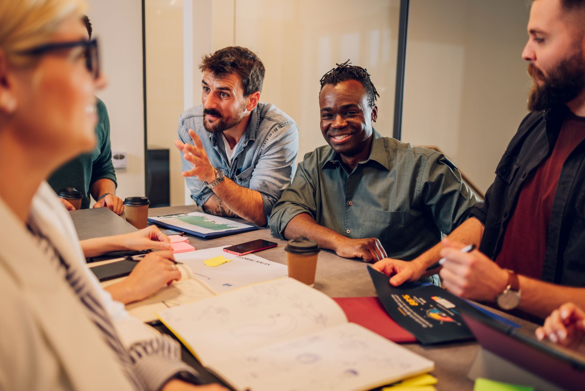 People in a business meeting, looking at documents. Man gestures while others listen.