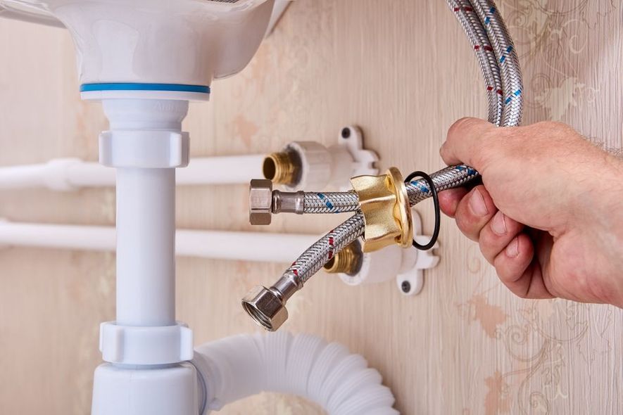 Hand tightening a brass plumbing valve under a sink with flexible hoses attached