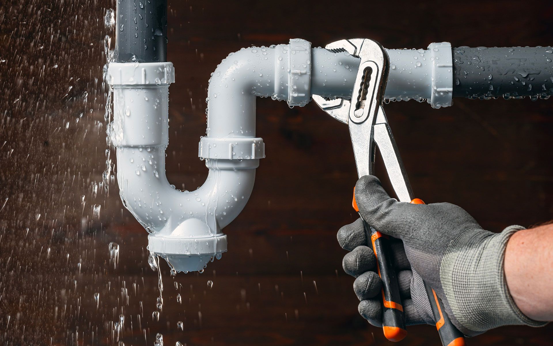 A plumber is fixing a leaking pipe with a wrench.