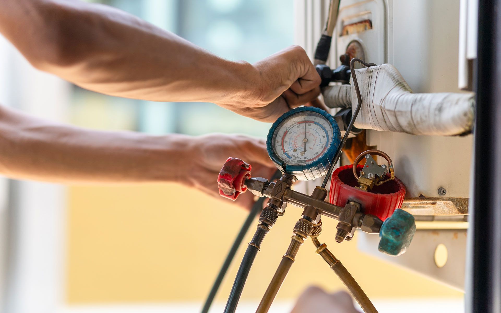 A man is working on an air conditioner with a pressure gauge.