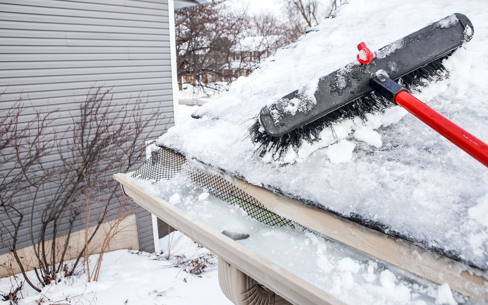 A person is brushing snow off a roof with a broom.