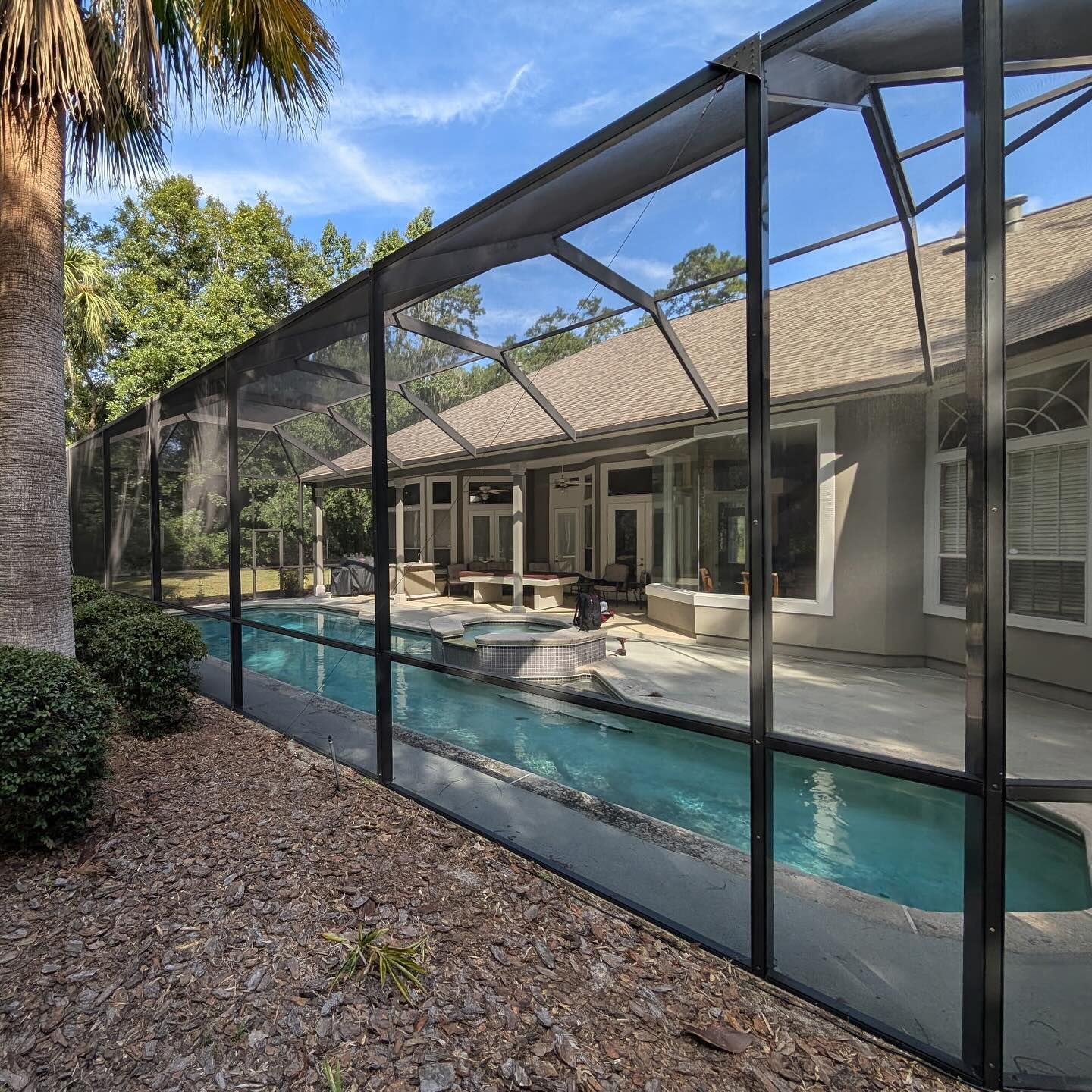 Screened backyard pool beside a patio and house, with lounge chairs and trees in the background