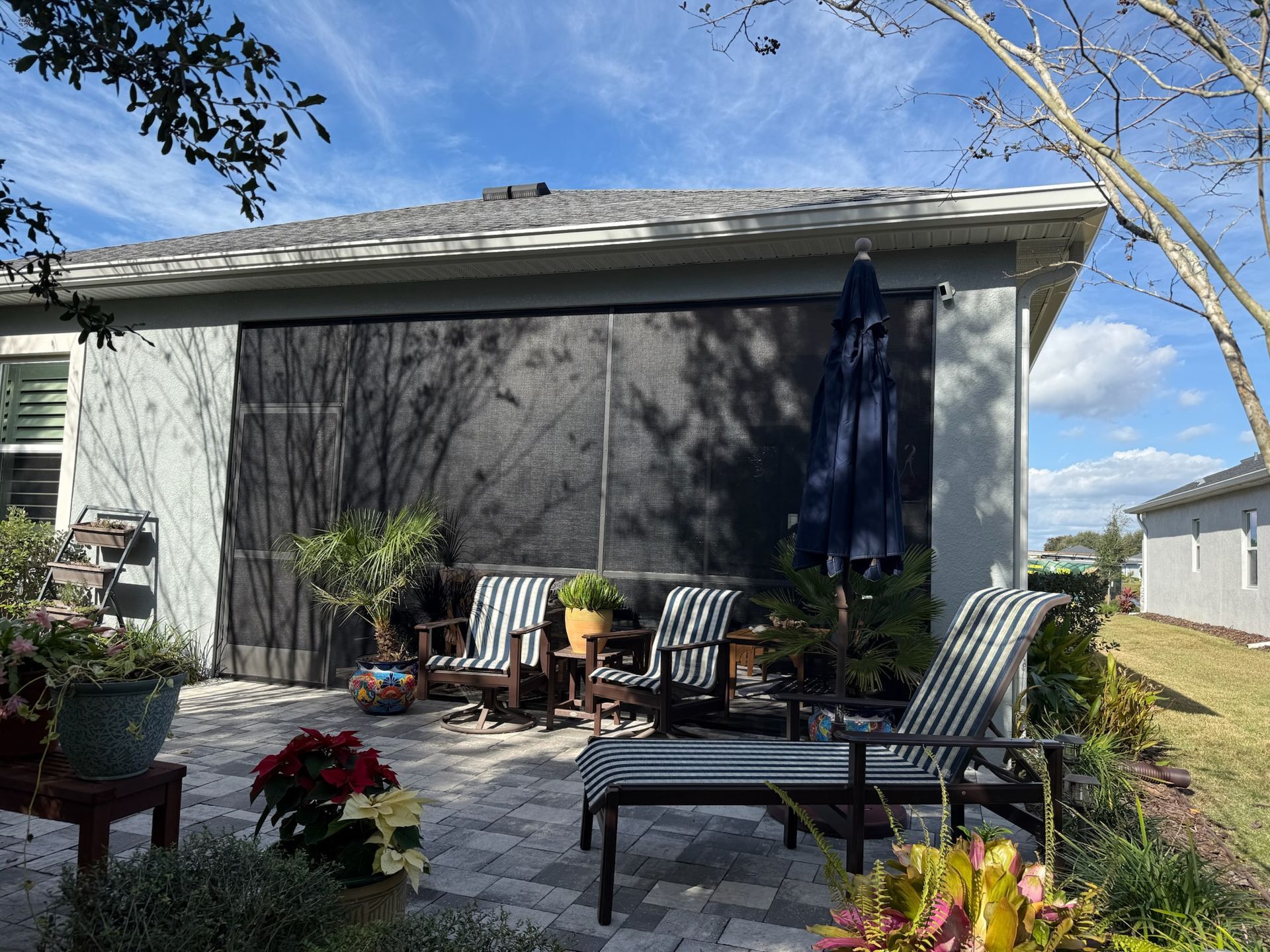 Patio with black screens, striped chairs, and potted plants under a blue sky.