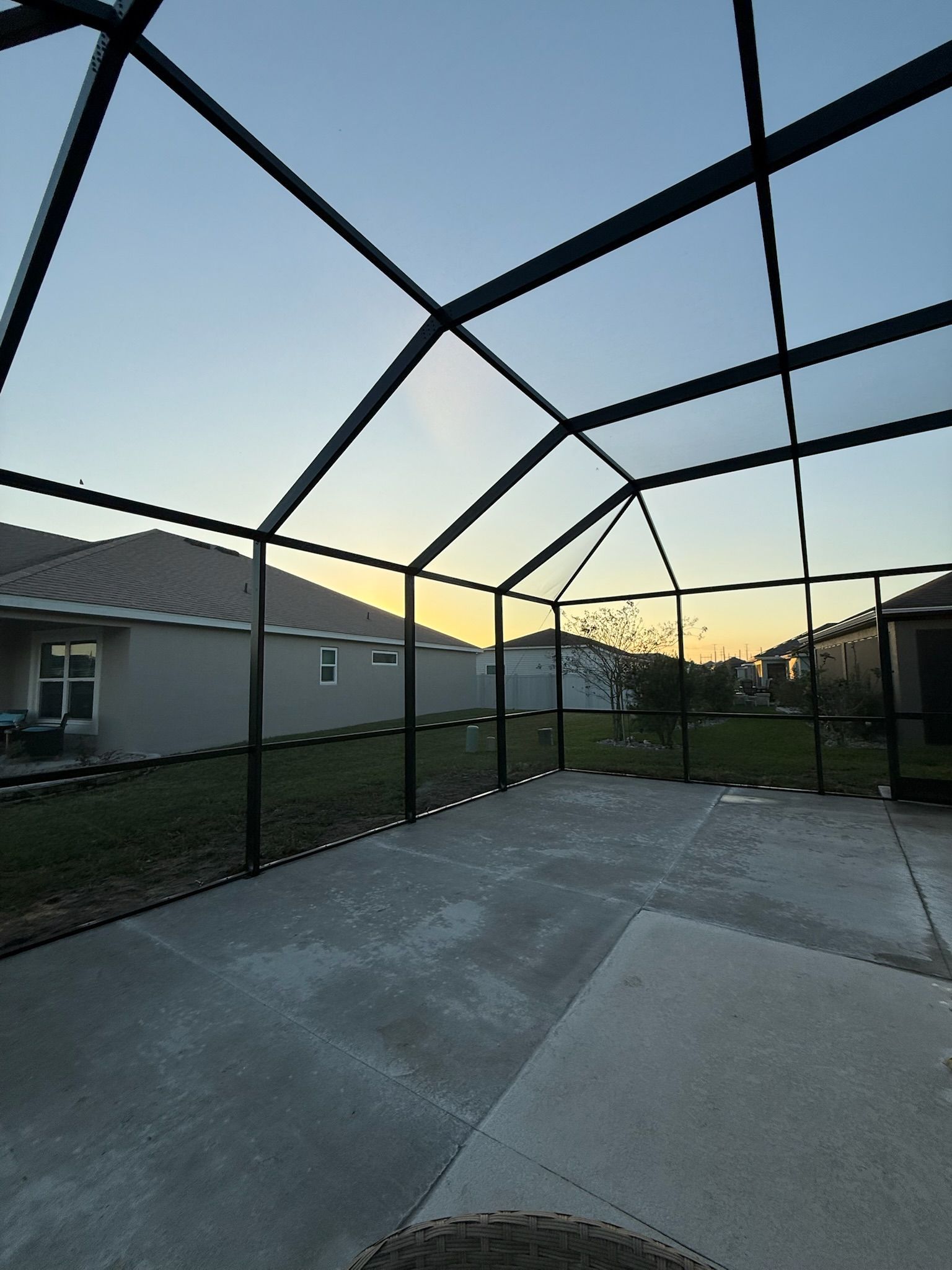 Patio enclosed by black screening, concrete floor, view of houses at dusk.