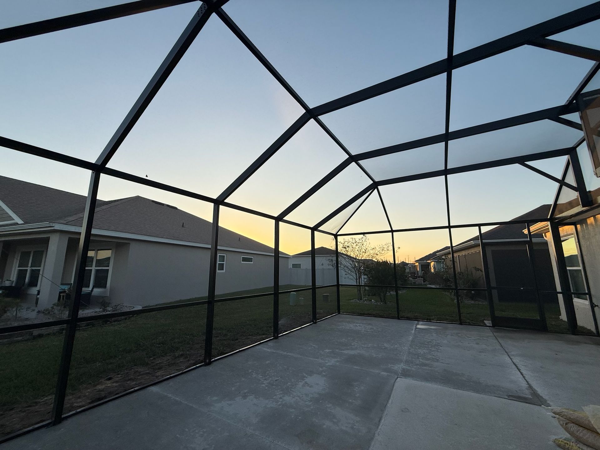Backyard screened patio at sunset with a concrete floor and black metal frame.