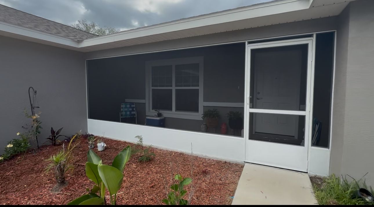 Screened-in porch with white trim and door. Red mulch in front, plants. Overcast sky.