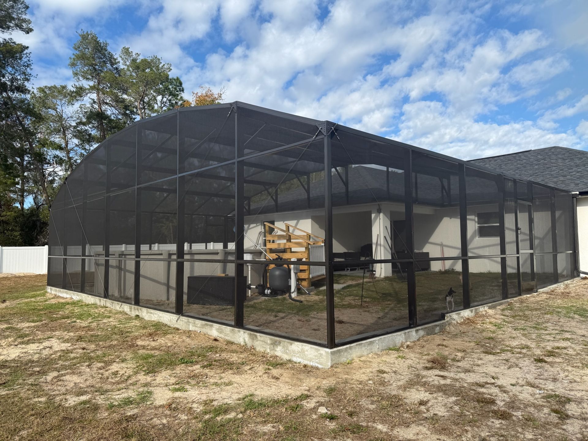 Screened patio enclosure attached to a house, with outdoor equipment inside and a cloudy blue sky.