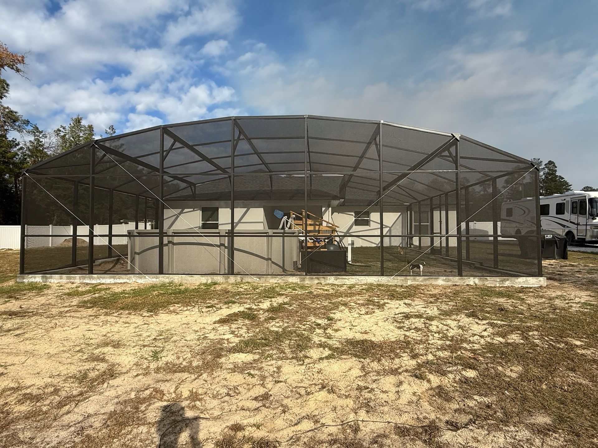 Metal animal enclosure with chain-link sides and roof in a sandy outdoor yard under a blue sky