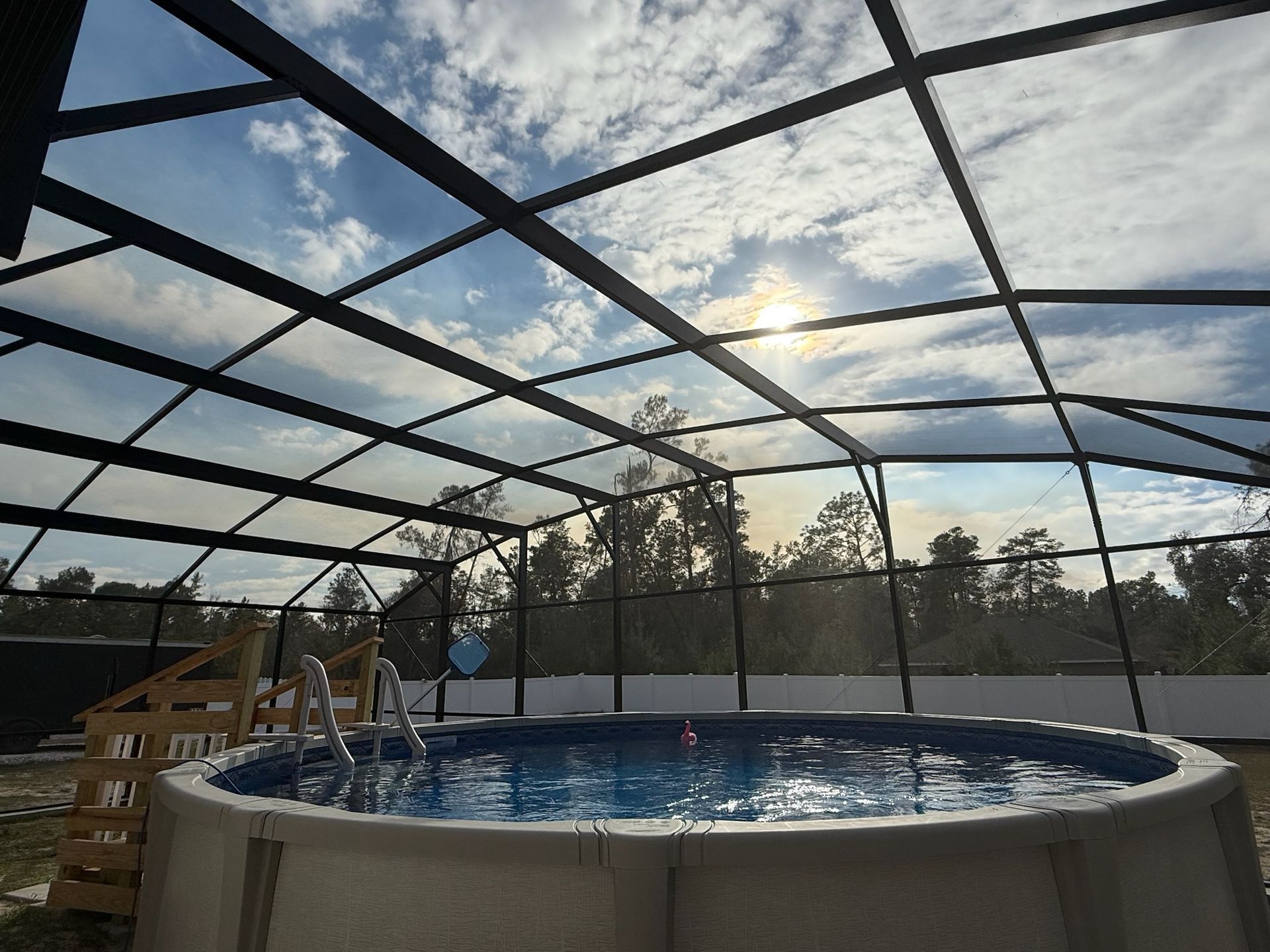 Covered backyard pool with a screened enclosure and lounge chairs under a cloudy sky