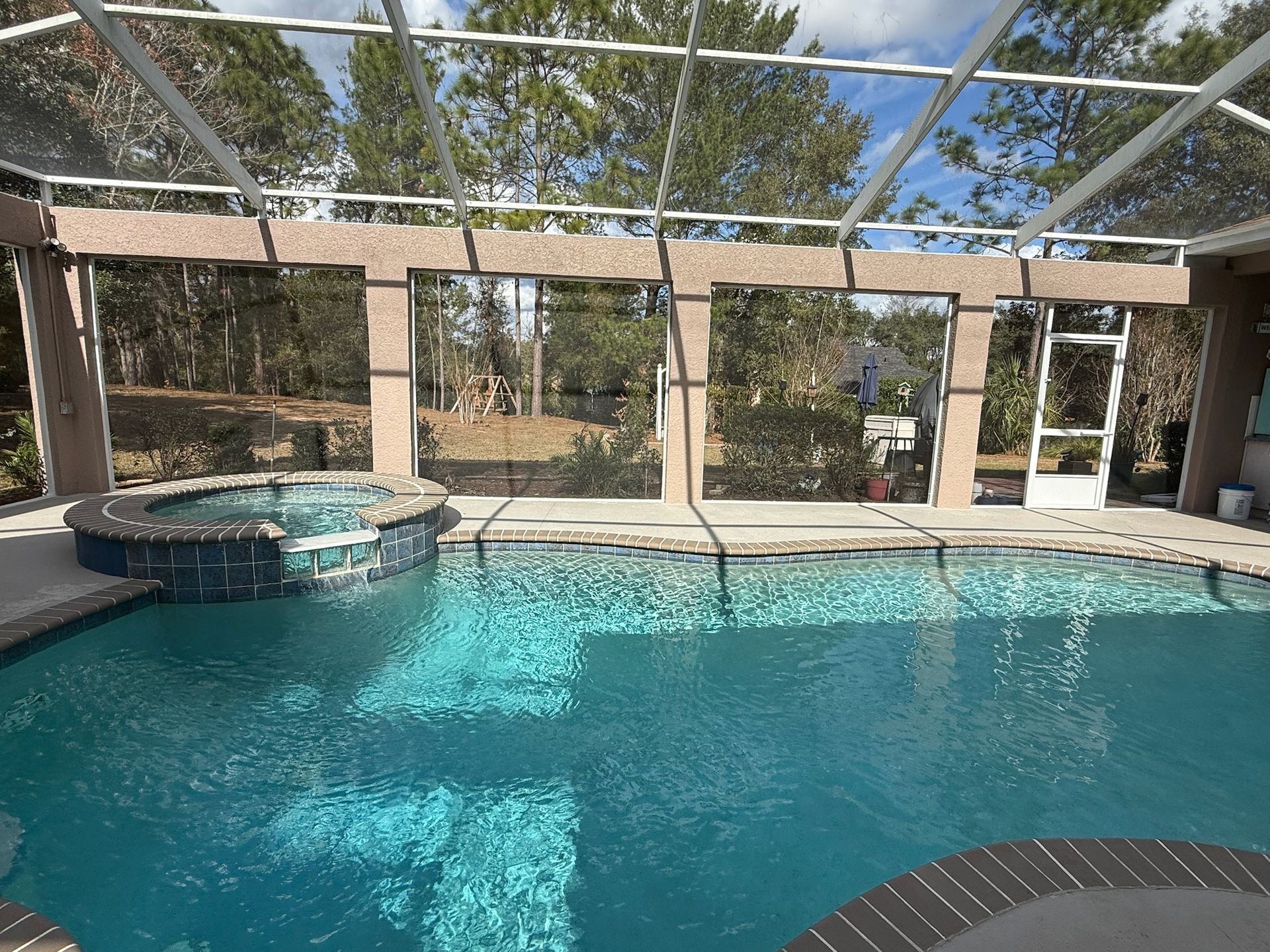 Screened indoor pool with blue water and attached hot tub under a glass ceiling.