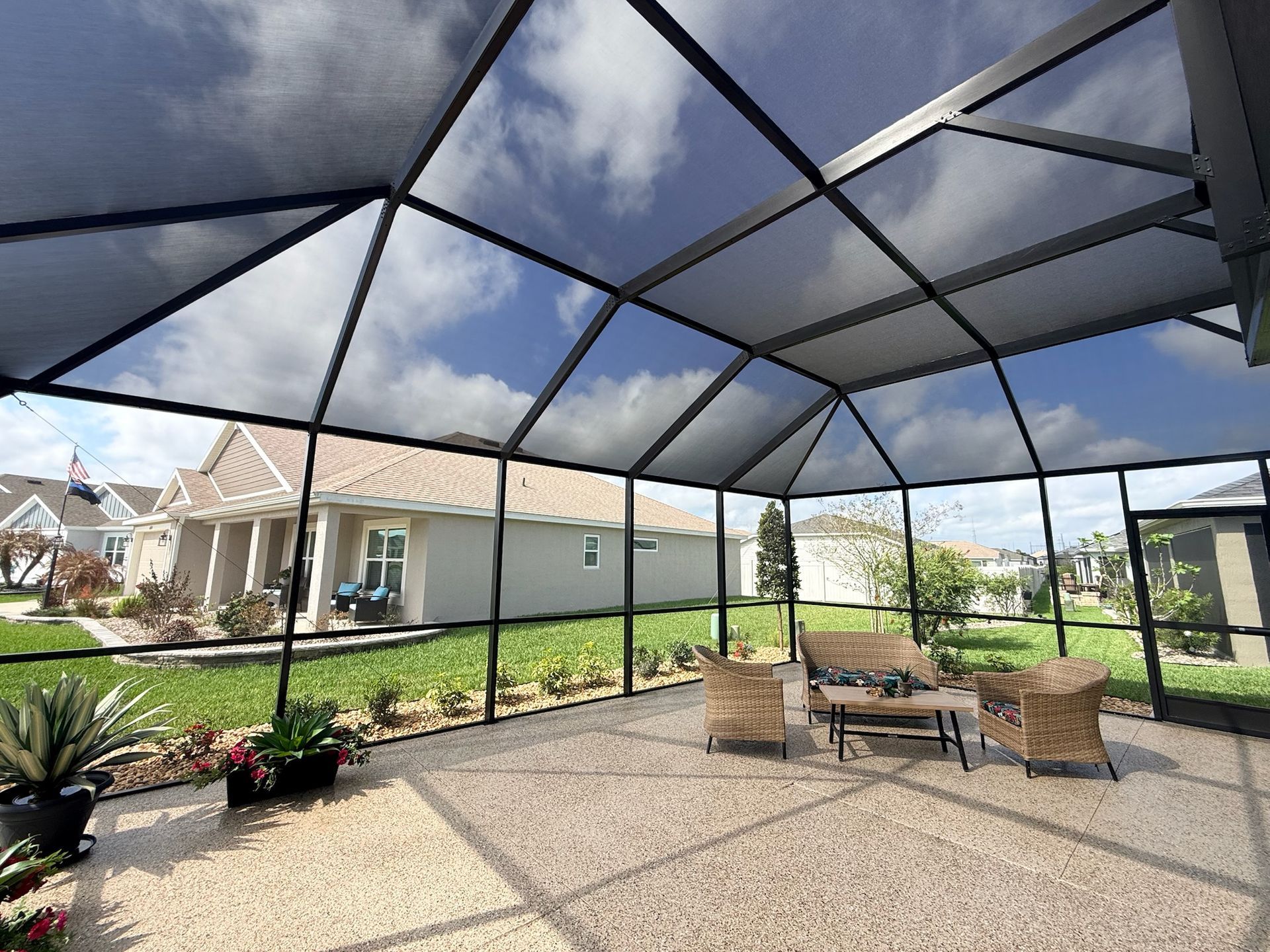 Screened-in patio enclosure with a bright sun, a house, and some trees.