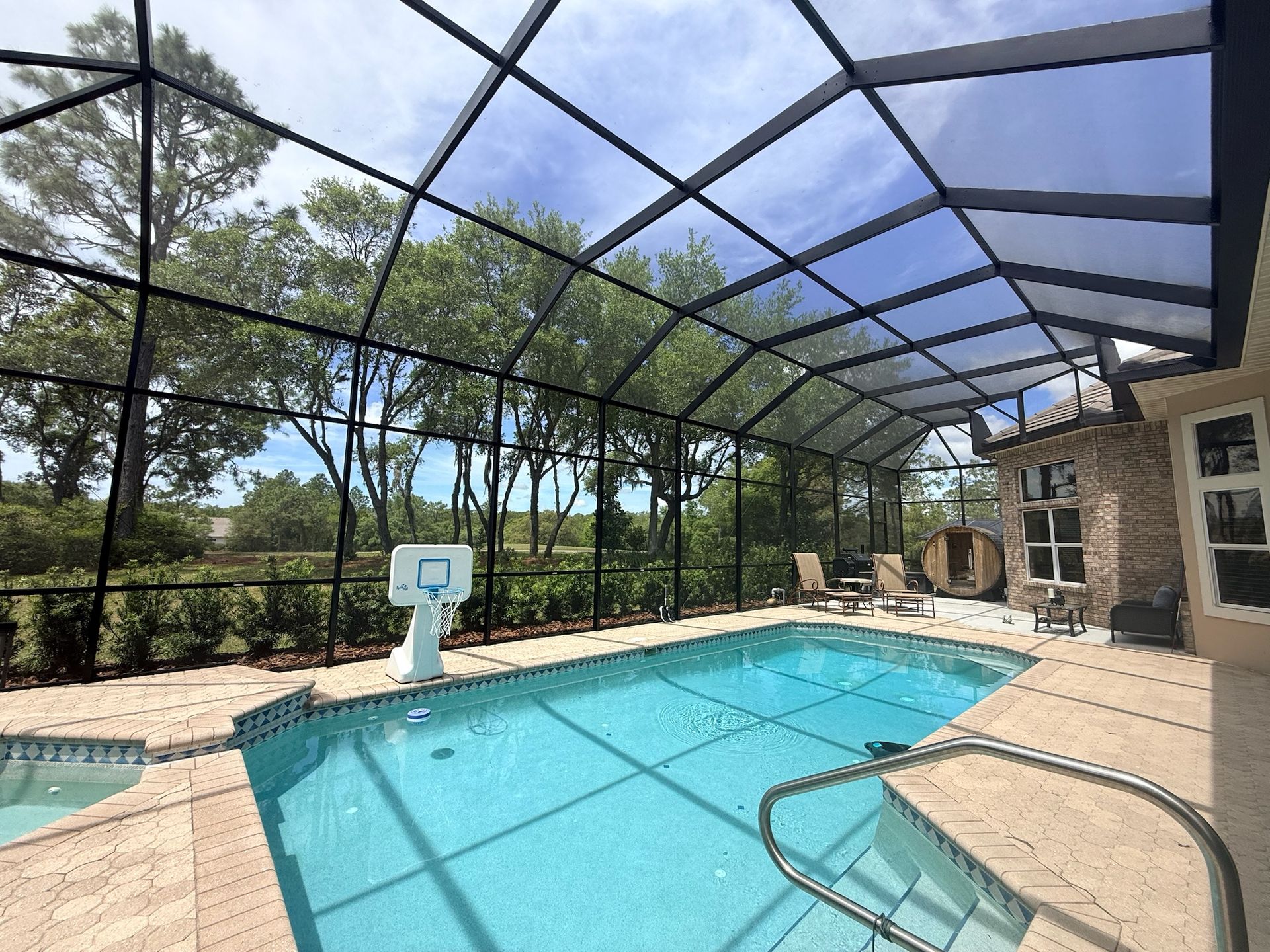 Pool enclosed by a black screen, surrounded by landscaping, with a house in the background.