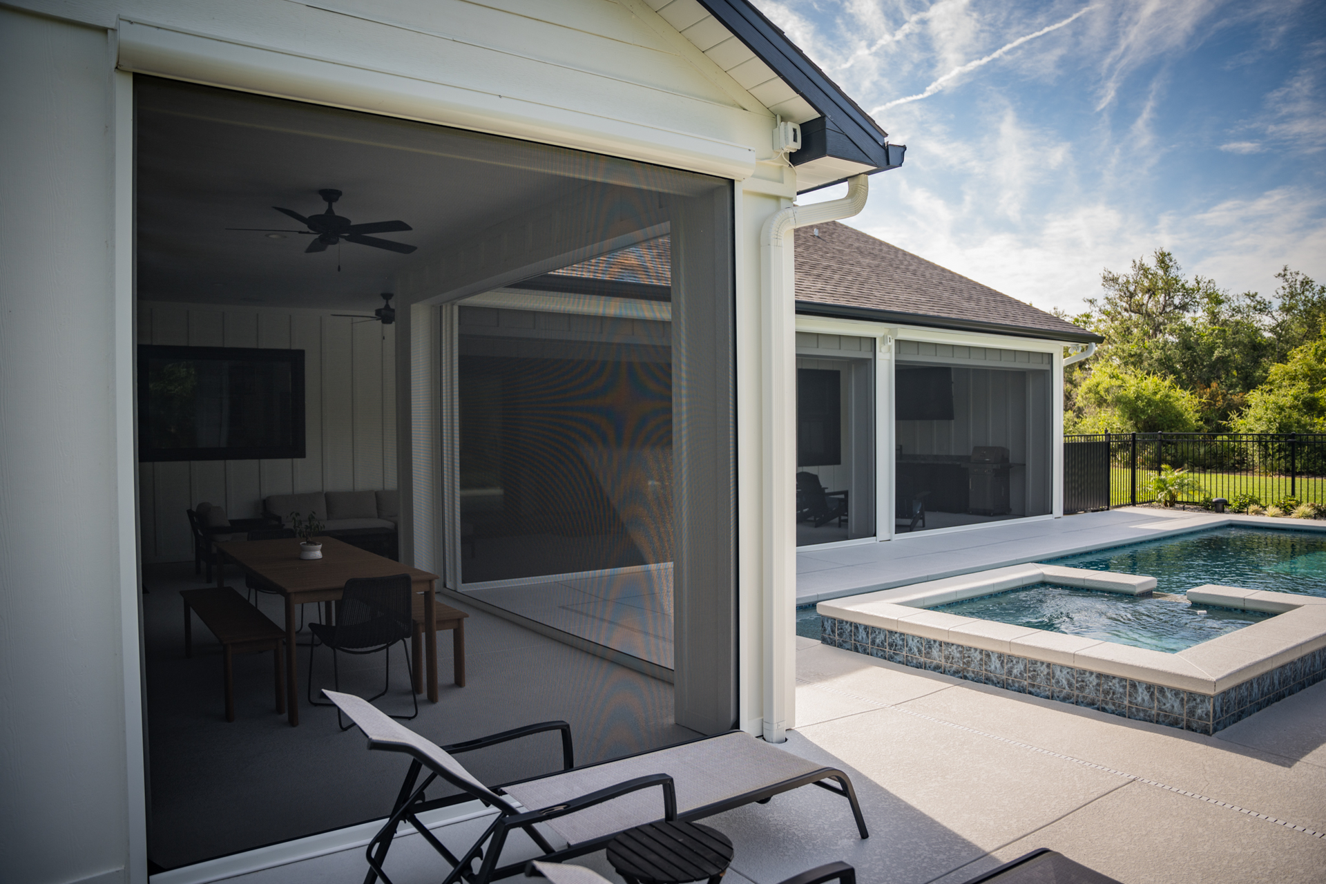 Covered patio beside a modern house, overlooking a sunlit backyard pool and lounge chairs