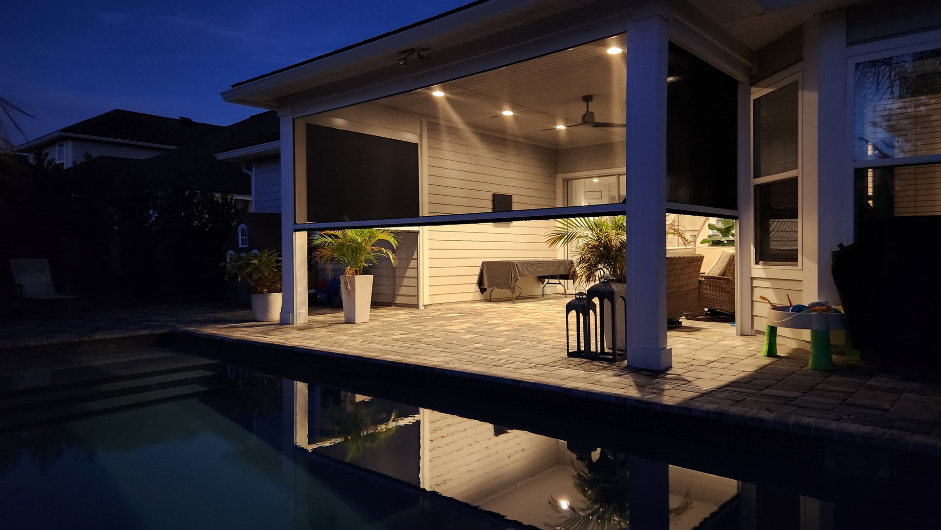 Modern patio with outdoor seating, warm lighting, and a pool reflecting the covered terrace at dusk
