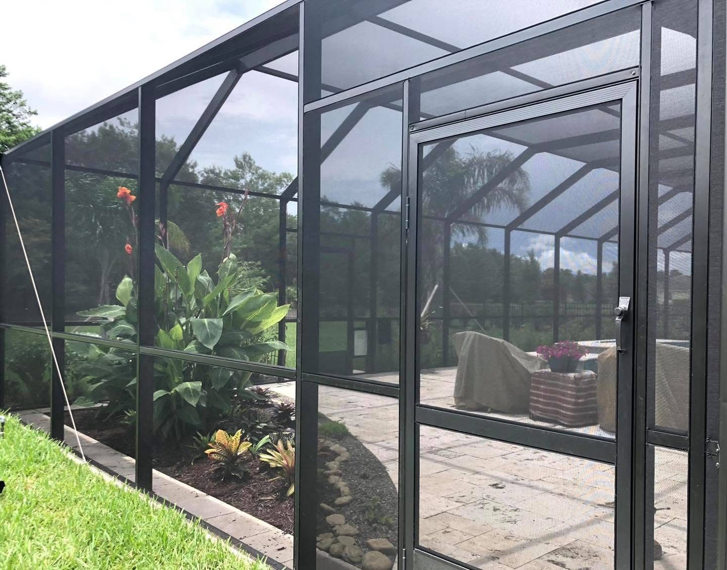Black screened-in patio enclosure with door; green plants and patio furniture visible.