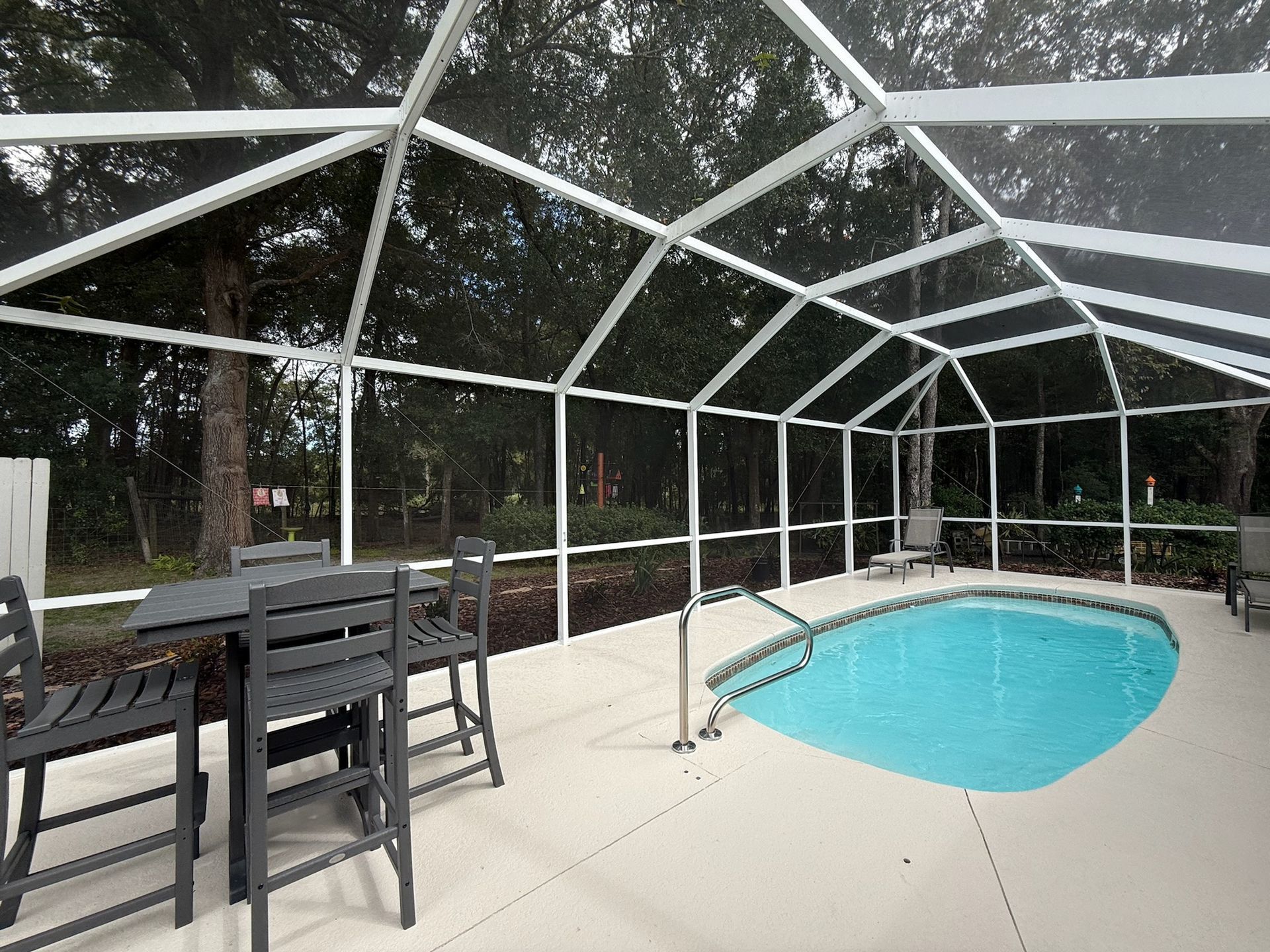 Screened-in pool area with turquoise water and patio furniture on a concrete deck