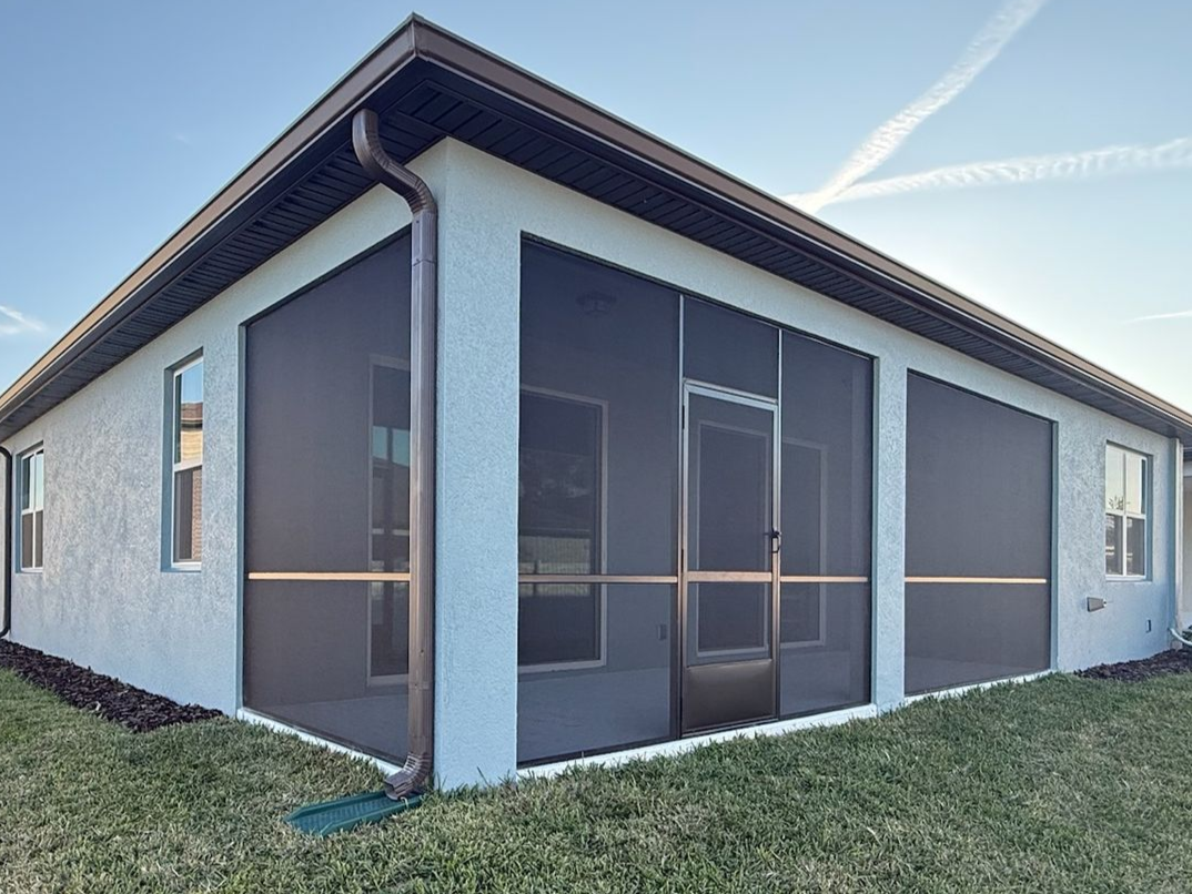 Backyard screened patio at sunset with a concrete floor and black metal frame.