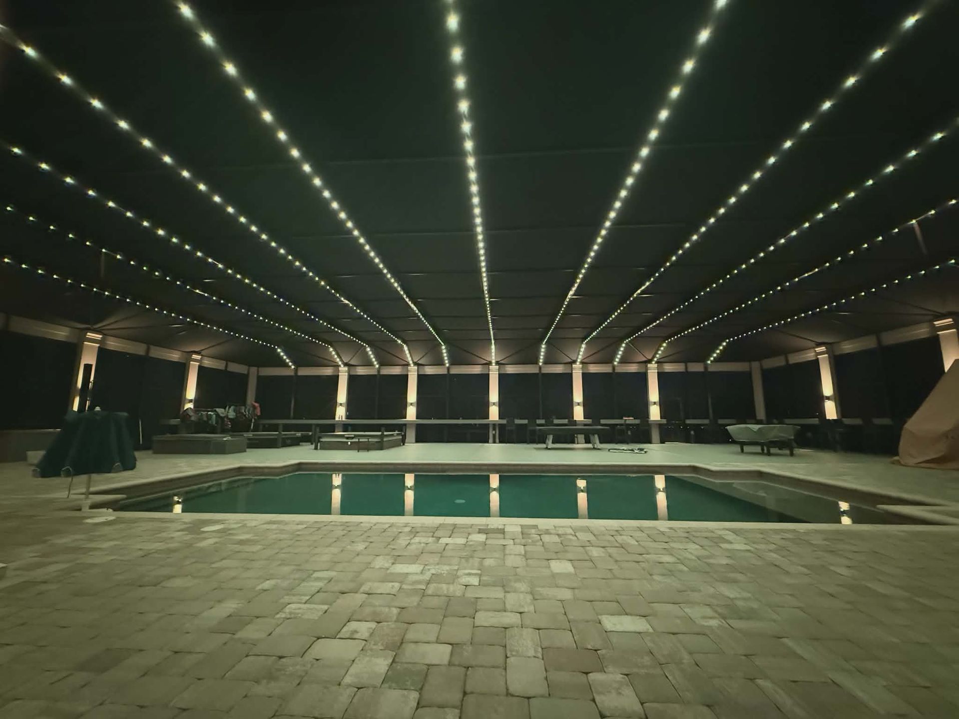 A covered swimming pool at night, lit by string lights on the ceiling.