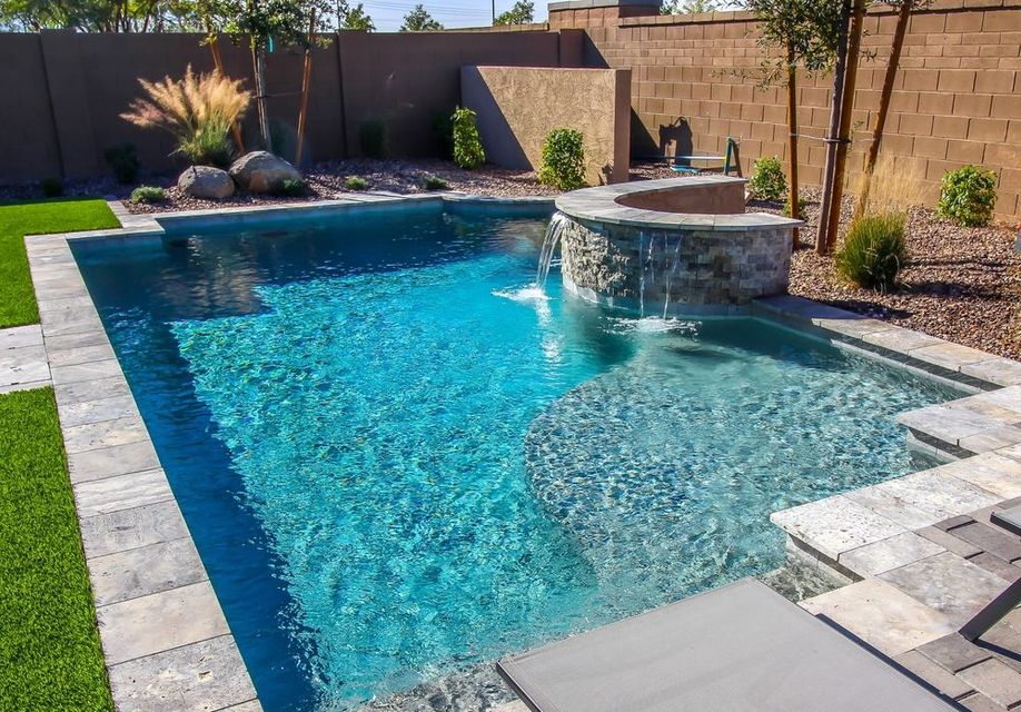 A large swimming pool with a waterfall in the backyard of a house.
