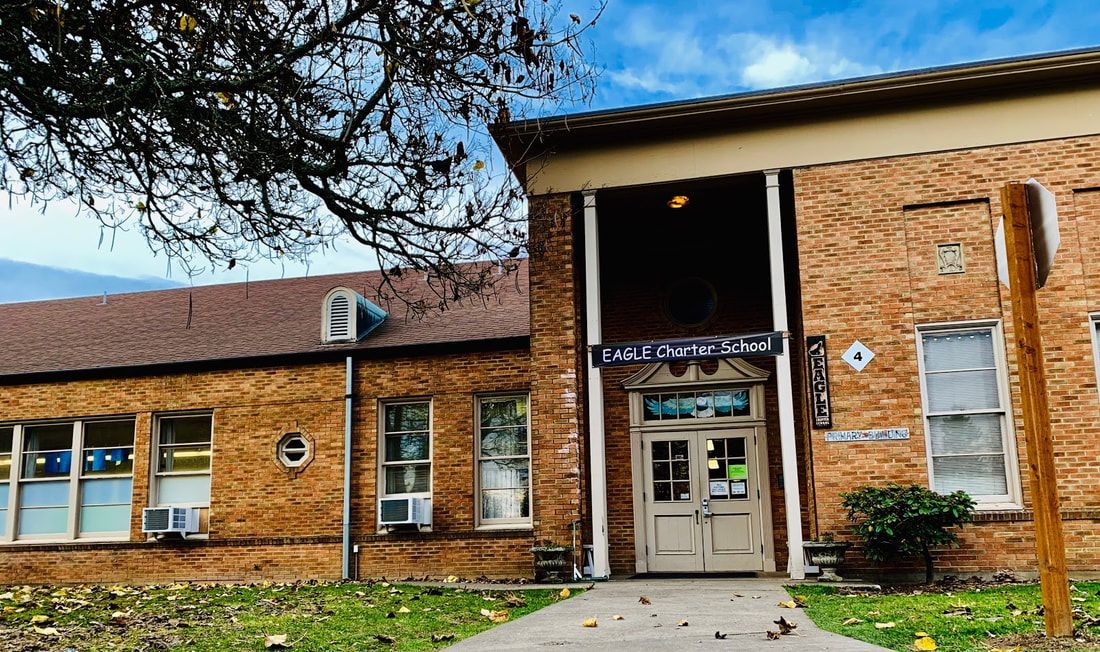 Front entry to a brick school building with a sidewalk and leading up to double doors.