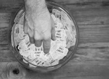 Black and white photo with a hand reaching into a glass bowl with raffle tickets picking one out.