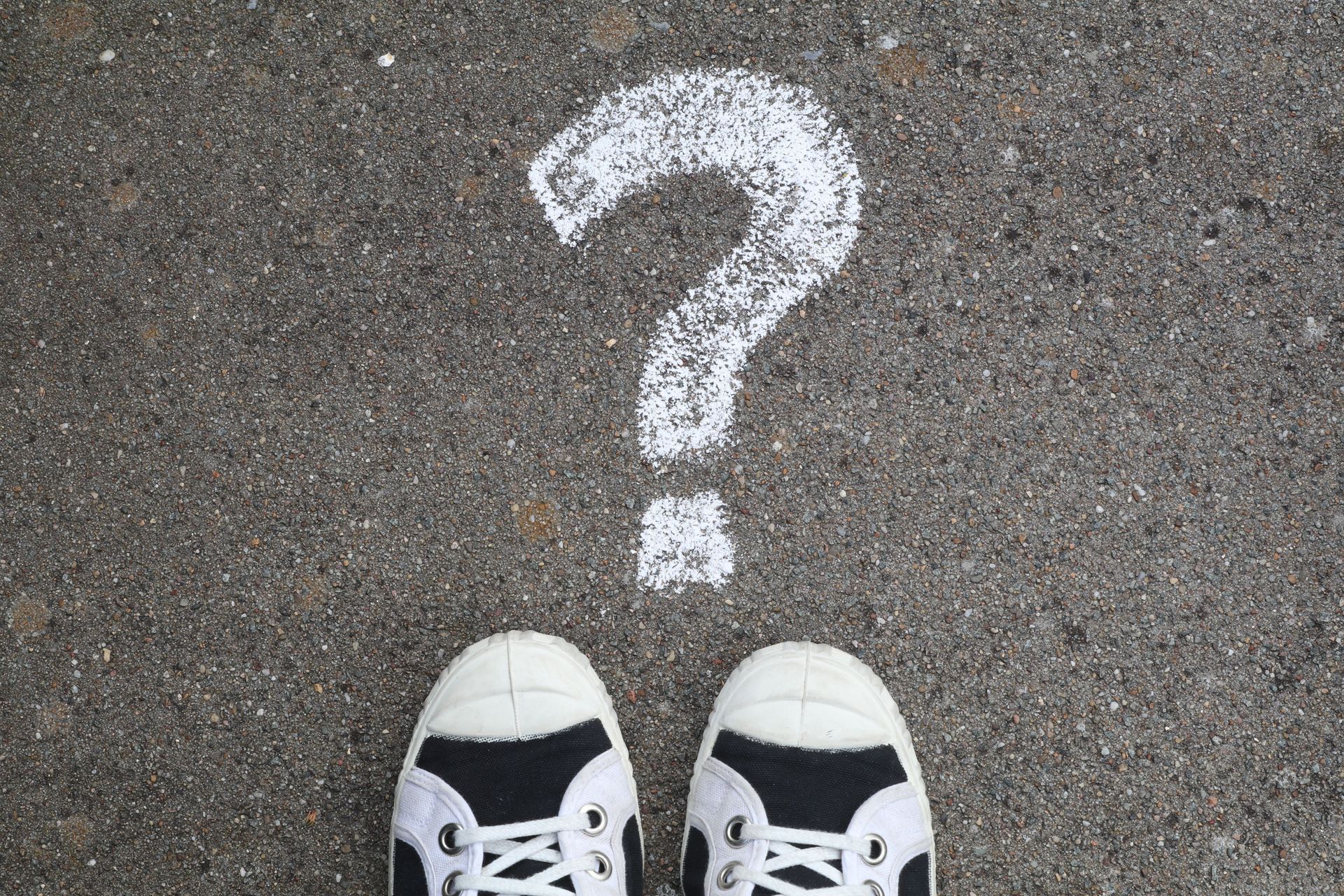 Point of view looking down at shoes on concreate with a chalk drawing of a question mark.