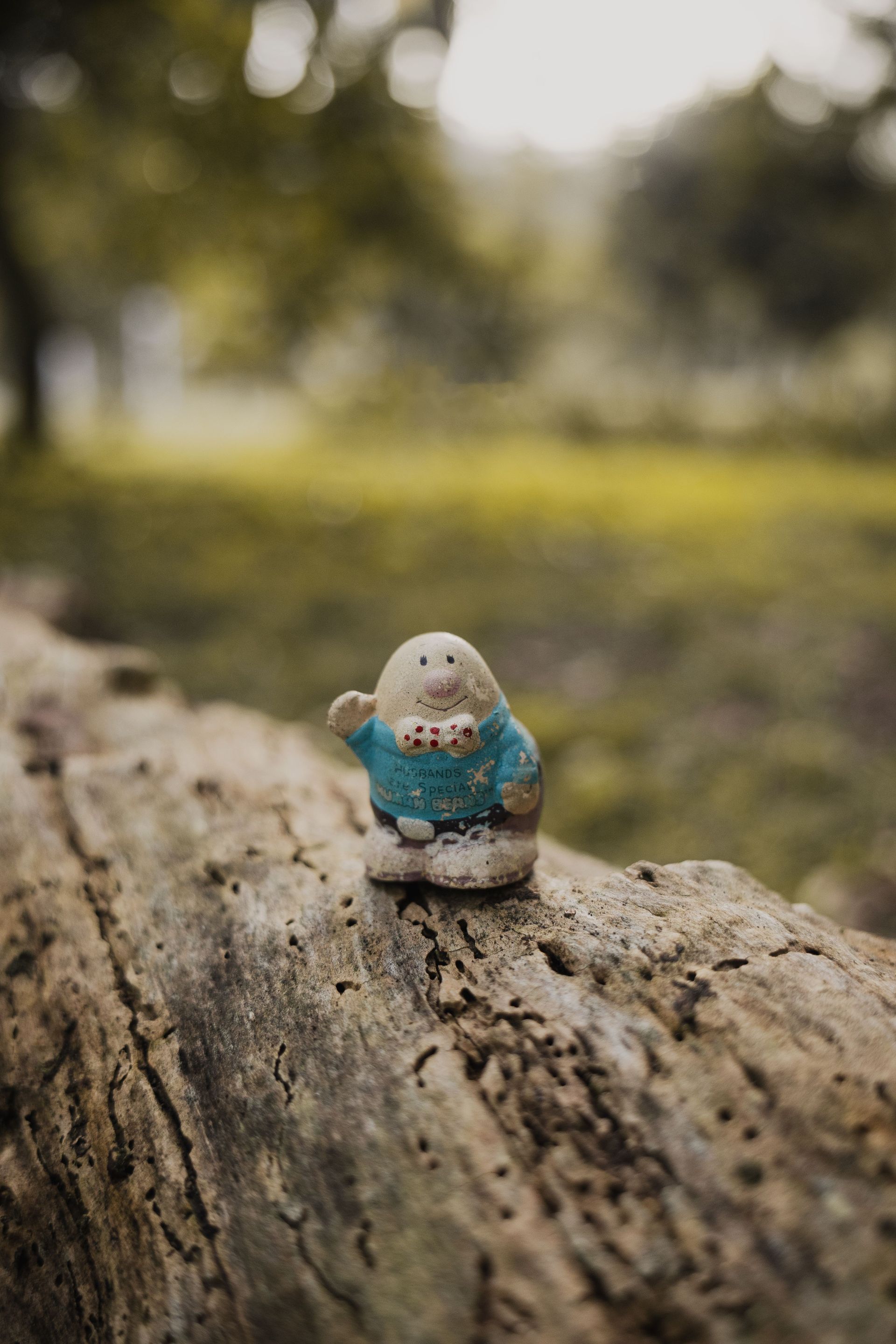 Cute ceramic figurine sitting on an old log.