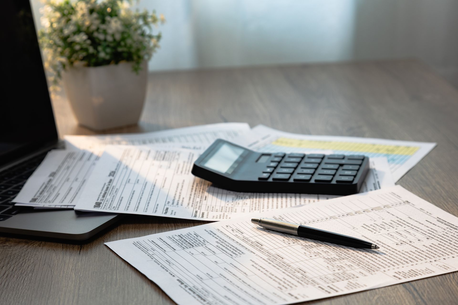 Workspace with tax papers, calculator, pen, laptop, and plant.