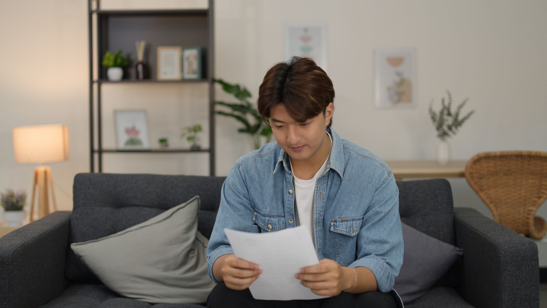 A focused man is reviewing paperwork needed for tax return preparation, while sitting on a sofa.