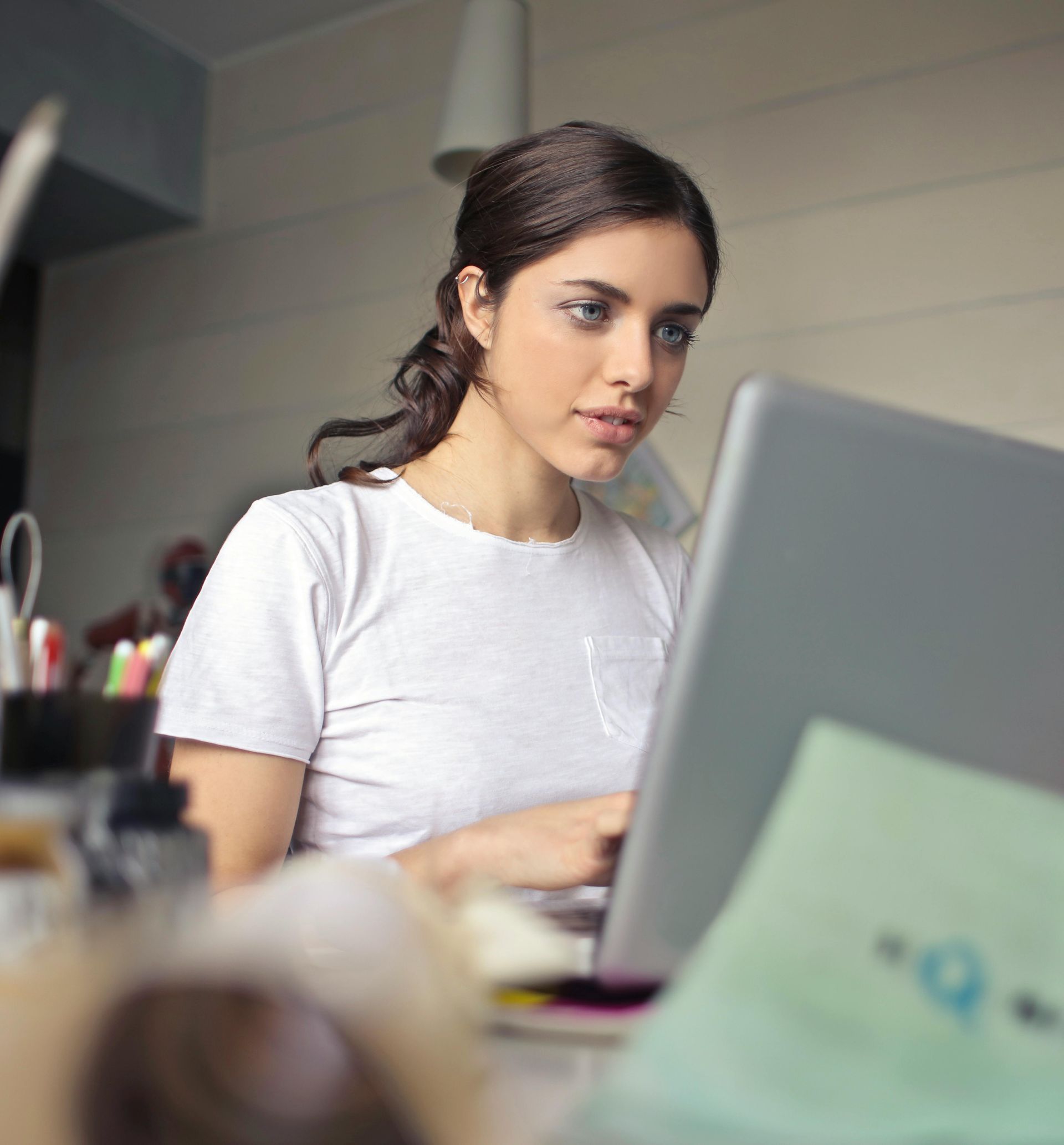 Woman working on a laptop at a desk, wearing a white shirt and looking intently.