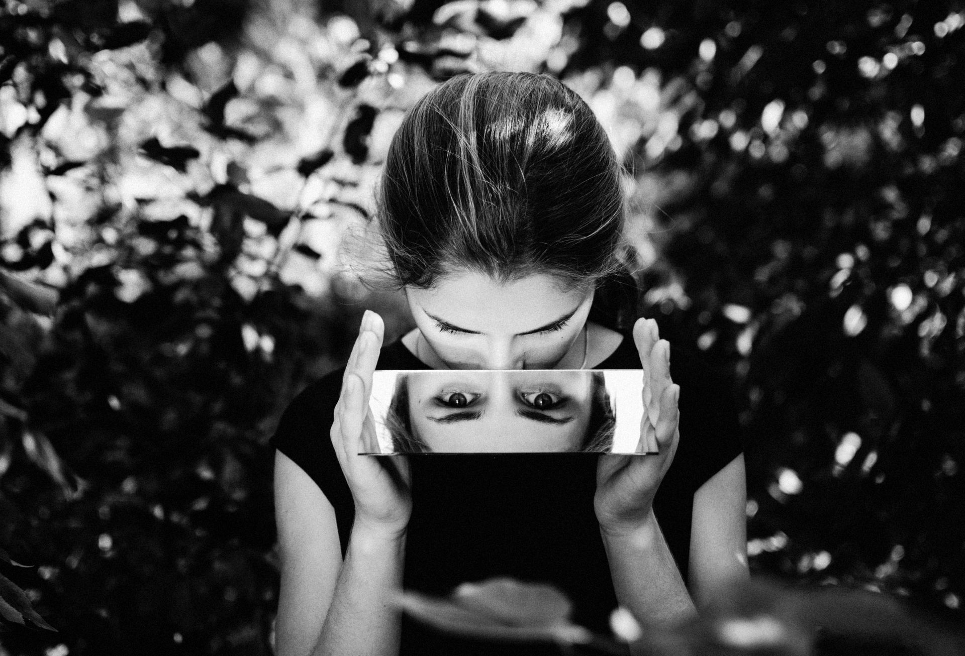 Woman holding mirror, reflecting her eyes in foliage background. Black and white.