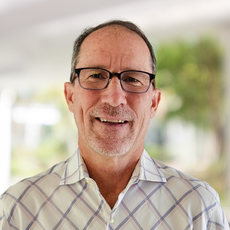 A man wearing glasses and a plaid shirt is smiling for the camera.