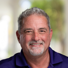 A man with a beard is wearing a purple shirt and smiling.