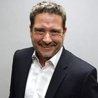 A man in a suit and white shirt is smiling for the camera.