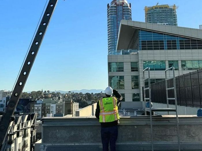 A man wearing a hard hat and safety vest is standing on top of a building looking out over a city.