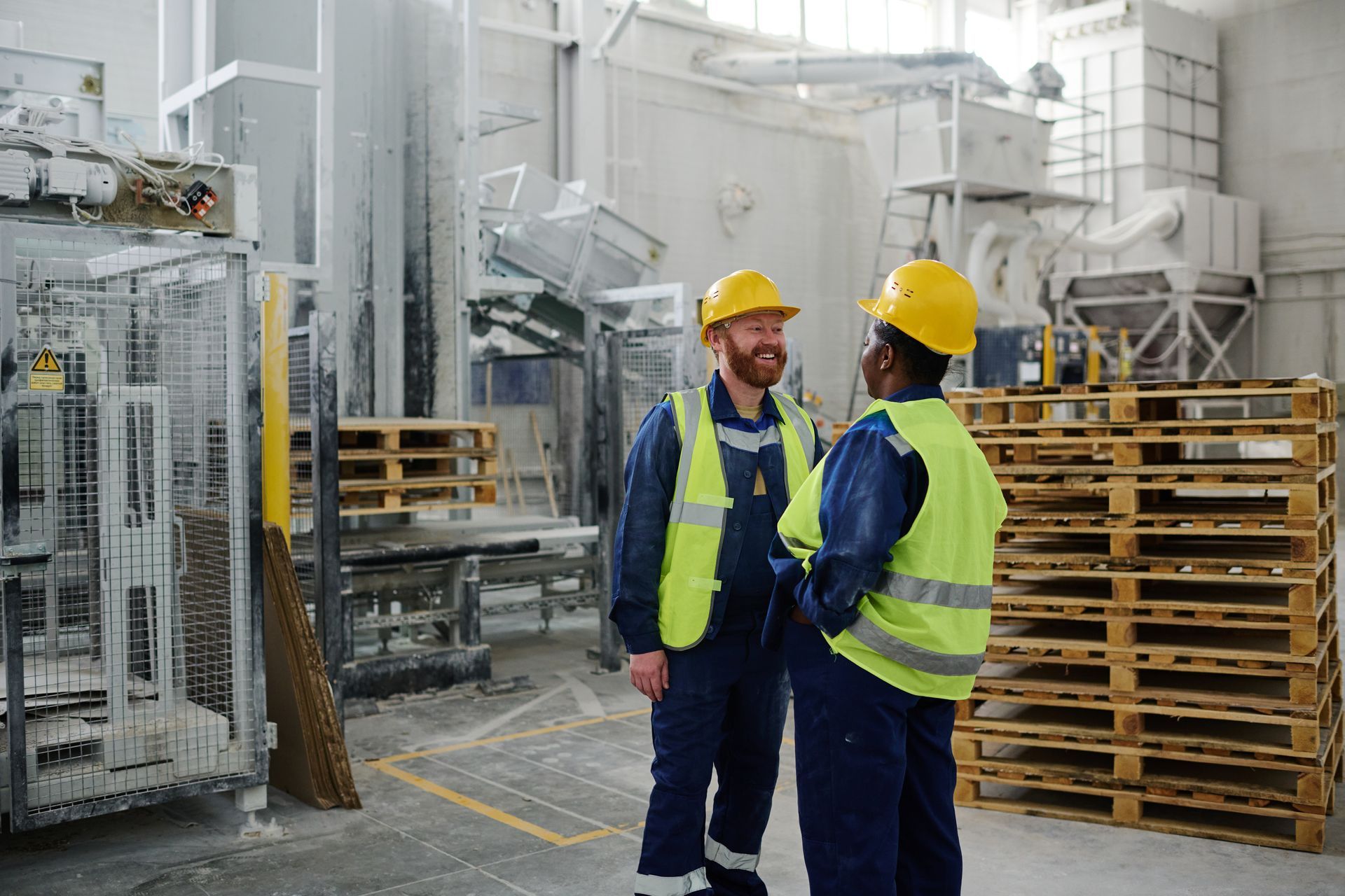 Two construction workers are shaking hands in a factory.