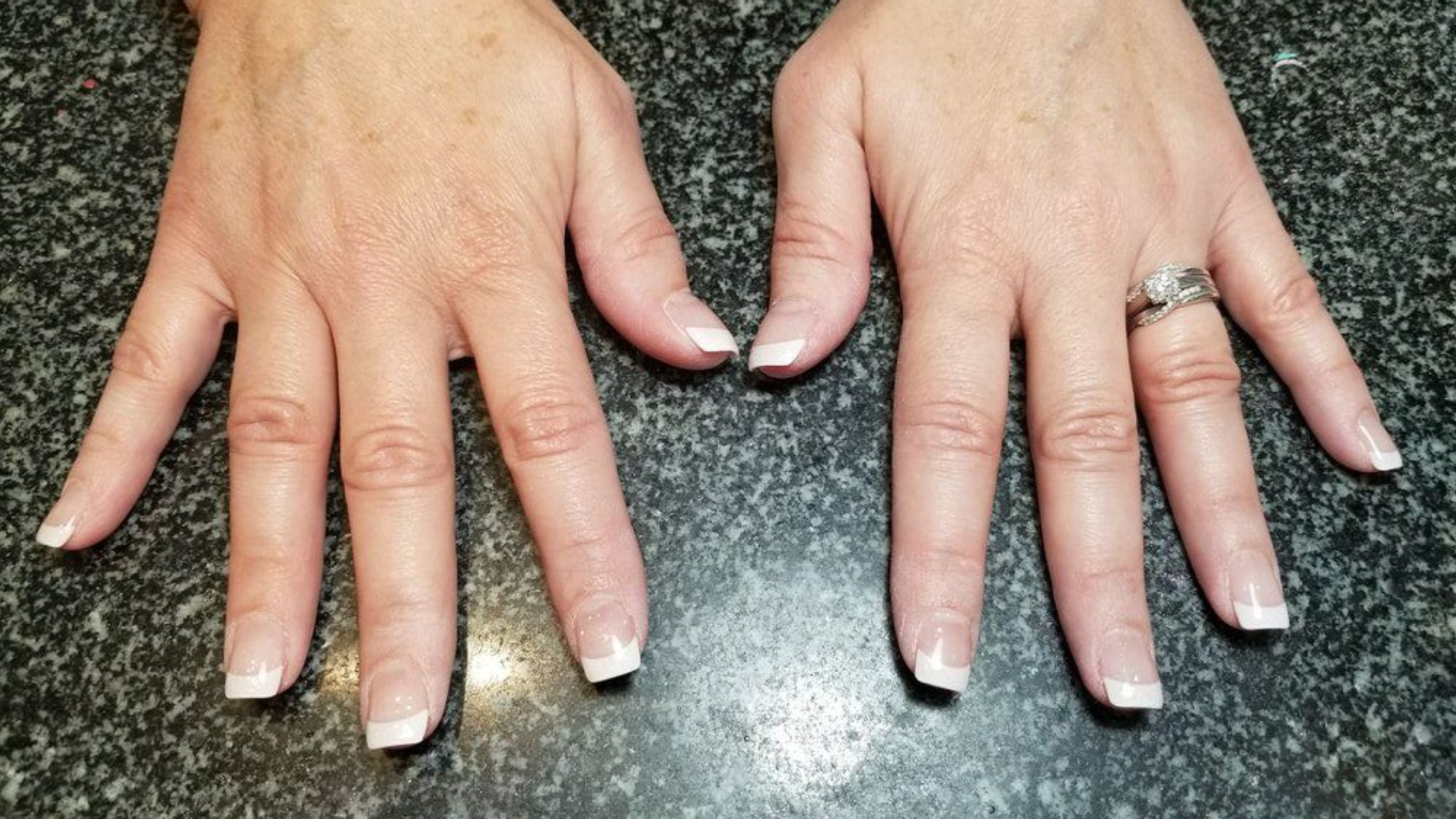 Two hands with French tip manicured nails. Ring on the ring finger.