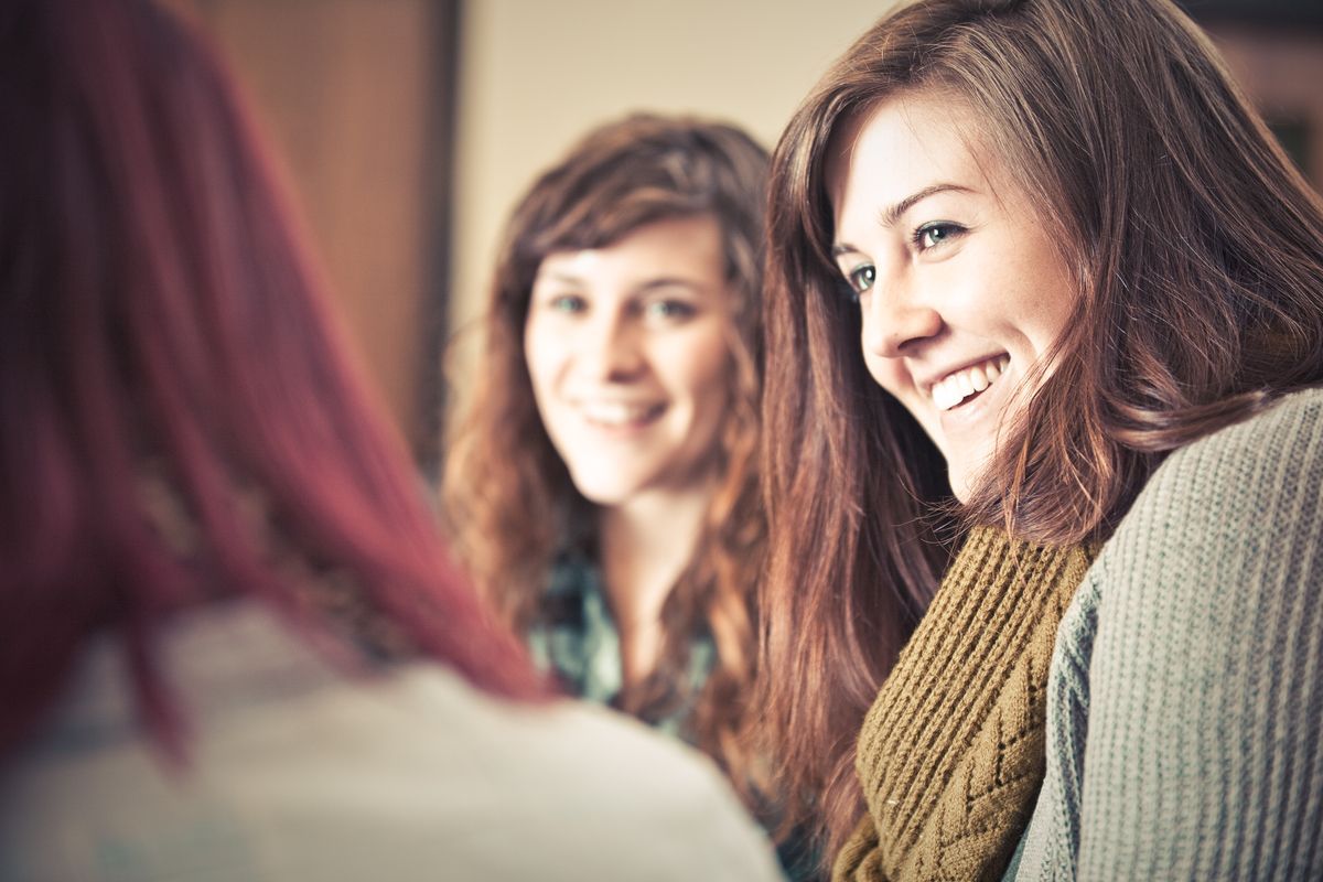 Three women smiling and talking in a softly lit indoor setting