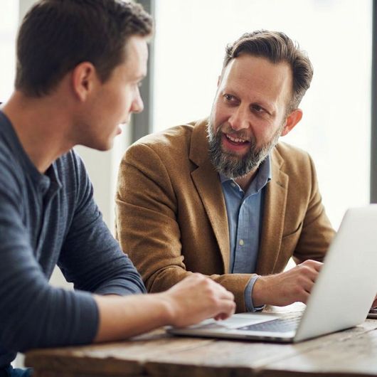 Two people discussing over a laptop at a table in a bright office