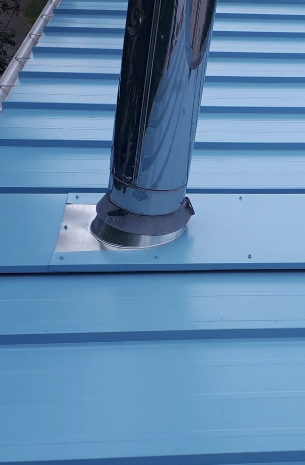 Une cheminée en acier inoxydable est posée sur un toit bleu.