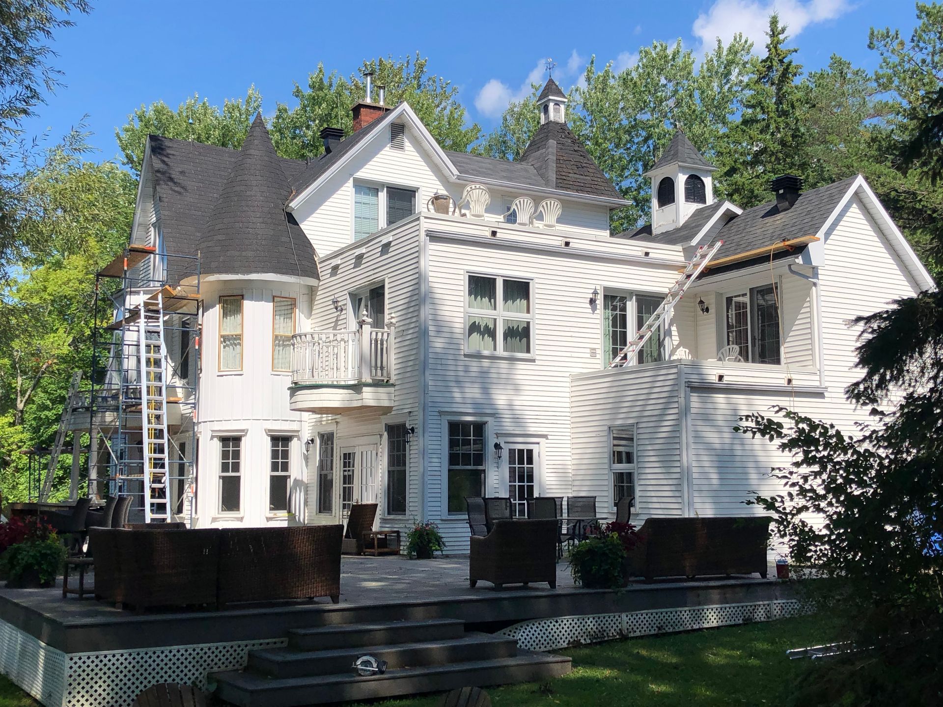 Une grande maison blanche avec un toit noir est entourée d'arbres.