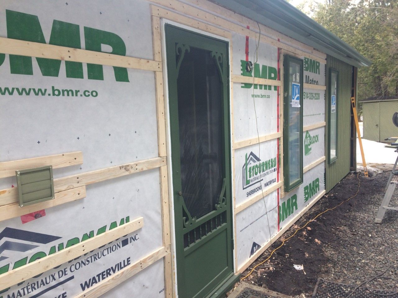 Un bâtiment avec une porte moustiquaire est en cours de construction par une entreprise appelée bmr