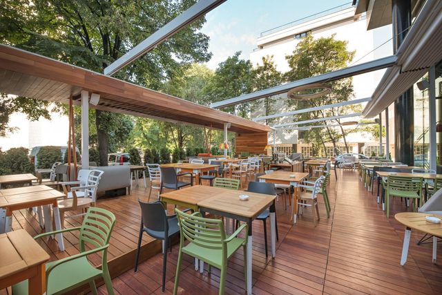 Swimming pool with two lounge chairs on wooden deck, surrounded by greenery under a blue sky.