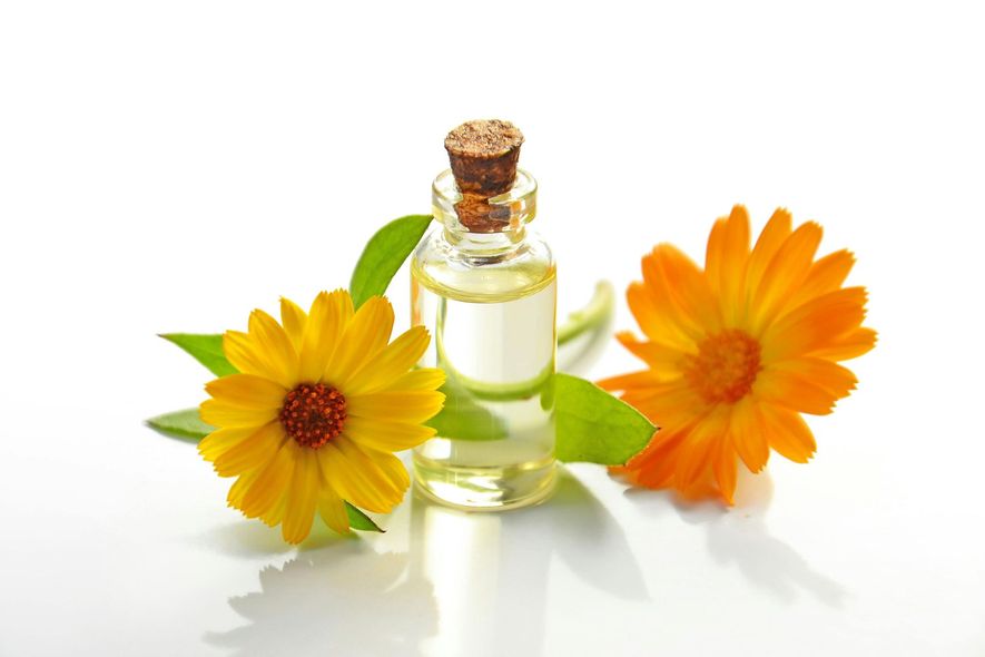 A bottle of essential oil next to two yellow flowers